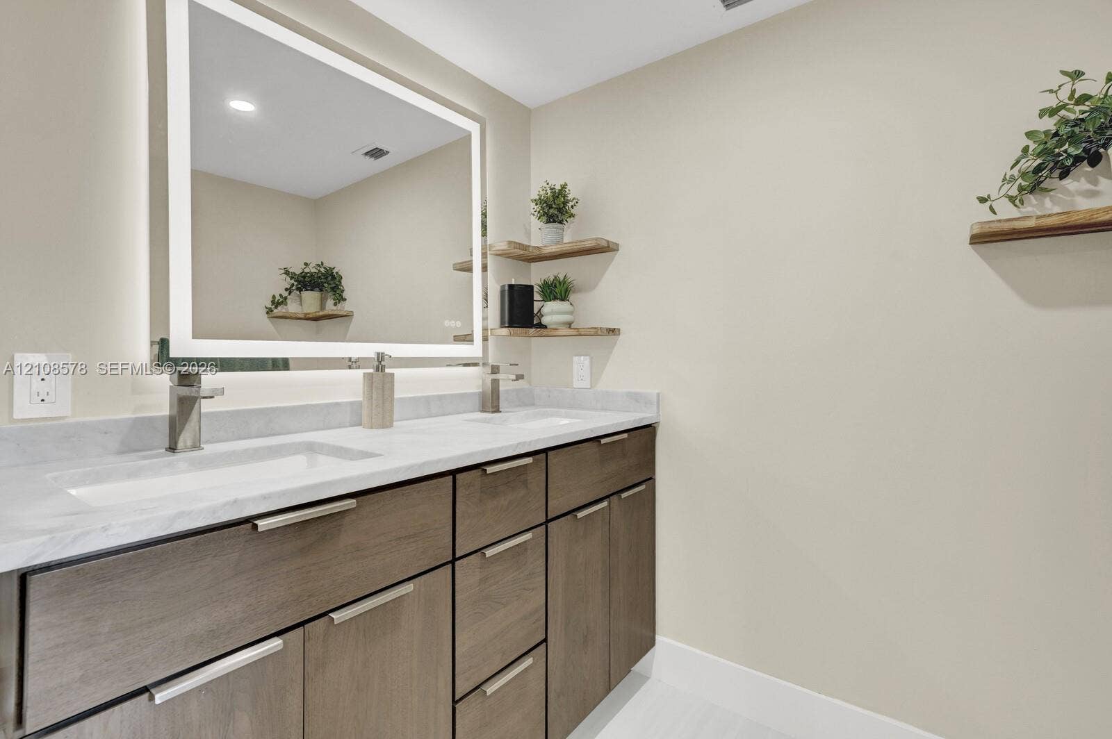 3005 Portofino Isle, #N2, Coconut Creek, Coconut Creek, FL 33066 Dual-sink vanity with stone-surfaced countertop, integrated backlit mirror, wood-finish cabinetry, and built-in wall shelving
