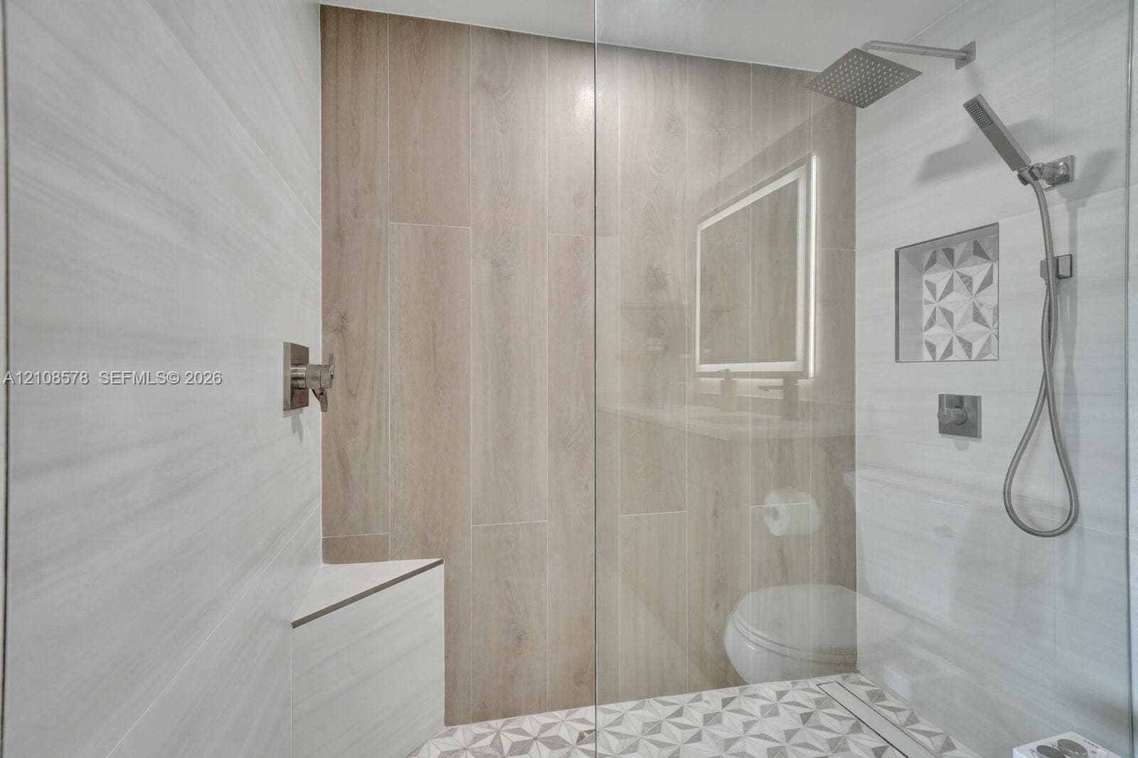 3005 Portofino Isle, #N2, Coconut Creek, Coconut Creek, FL 33066 Walk-in shower featuring wood-finish tile surround, a built-in corner bench, a rainfall showerhead with a handheld sprayer, and a decorative tile-lined wall niche