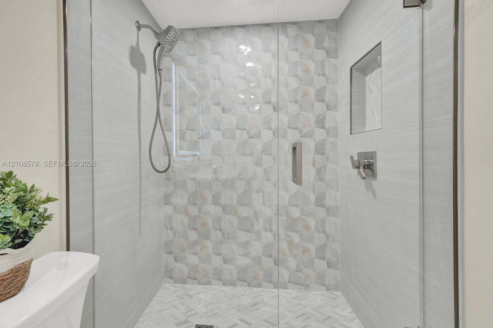 3005 Portofino Isle, #N2, Coconut Creek, Coconut Creek, FL 33066 Walk-in shower featuring a frameless glass door, geometric patterned accent tile, built-in wall niche, herringbone floor tile, and multi-setting handheld shower head