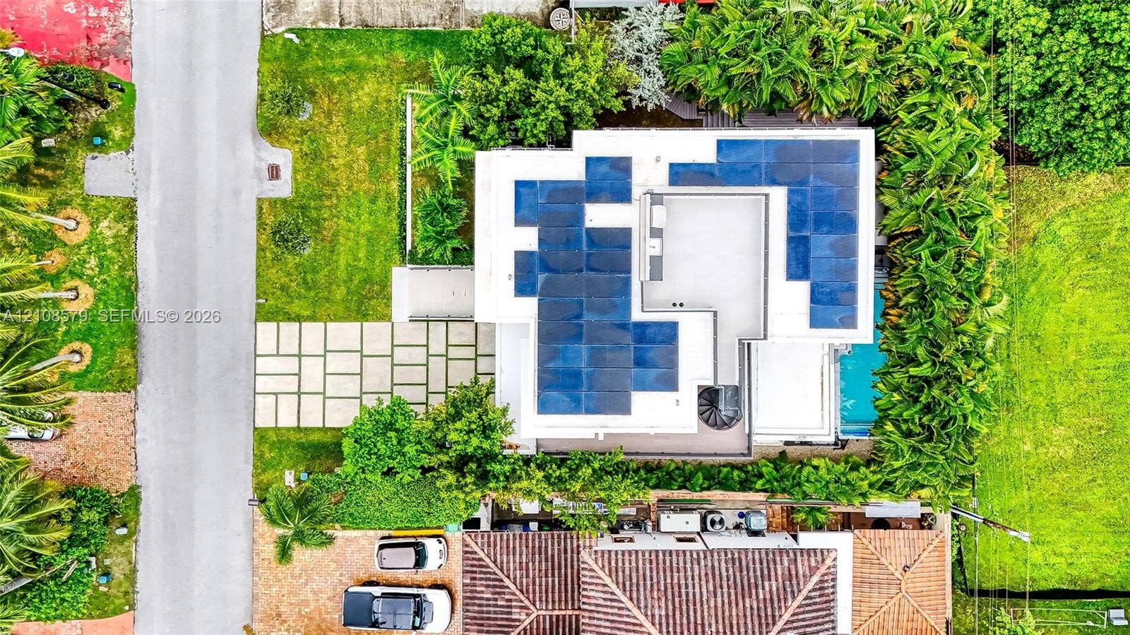311 189th Street, #0, Sunny Isles Beach, Sunny Isles Beach, FL 33160 Aerial perspective featuring a flat-roof residence equipped with a solar panel array, paved concrete grid driveway, perimeter landscaping, and a ground-level swimming pool