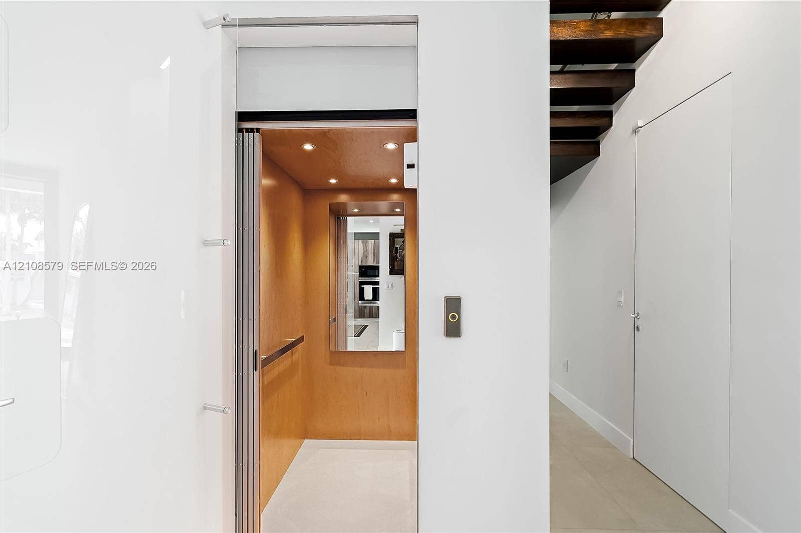 311 189th Street, #0, Sunny Isles Beach, Sunny Isles Beach, FL 33160 Residential elevator featuring a wood-paneled interior, recessed lighting, and a mirrored wall, complemented by an open-riser staircase with dark wood treads and neutral stone flooring