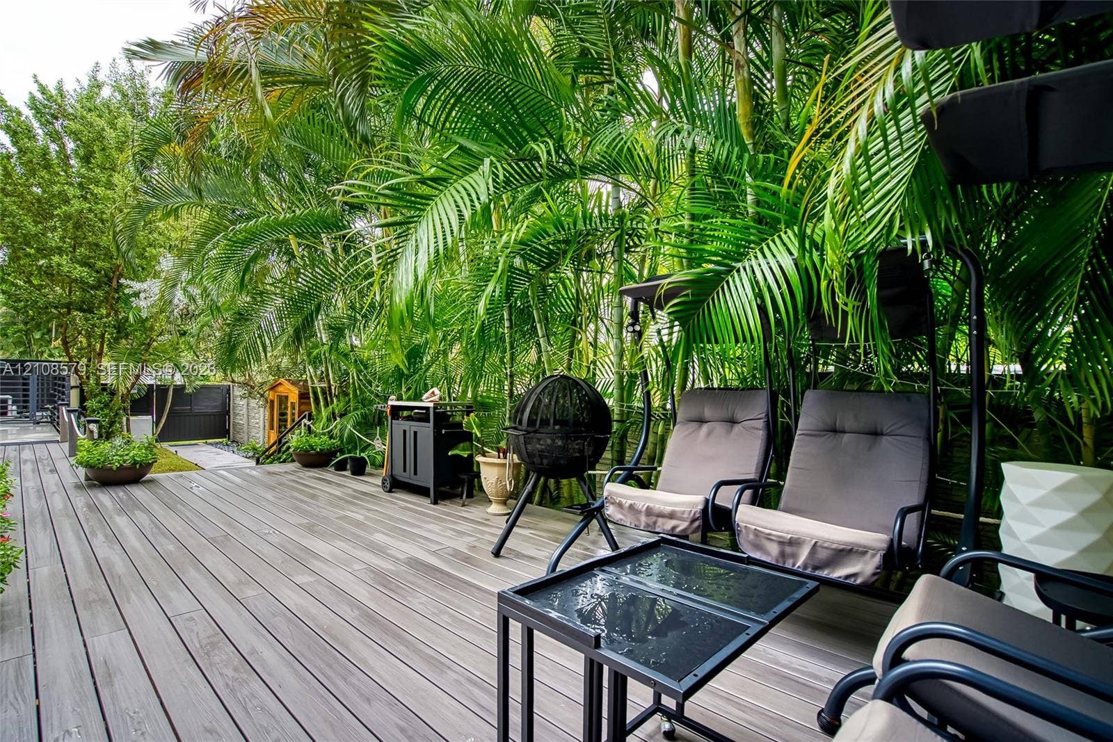 Expansive wood-finish decking featuring perimeter privacy landscaping with mature palms