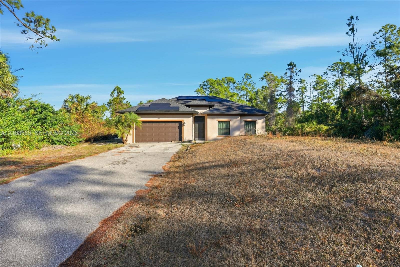 2363 NE 20 Th Avenue, Naples, FL 34120 Single-story exterior featuring a concrete driveway, two-car garage, hip roof with installed solar panels, and stucco siding