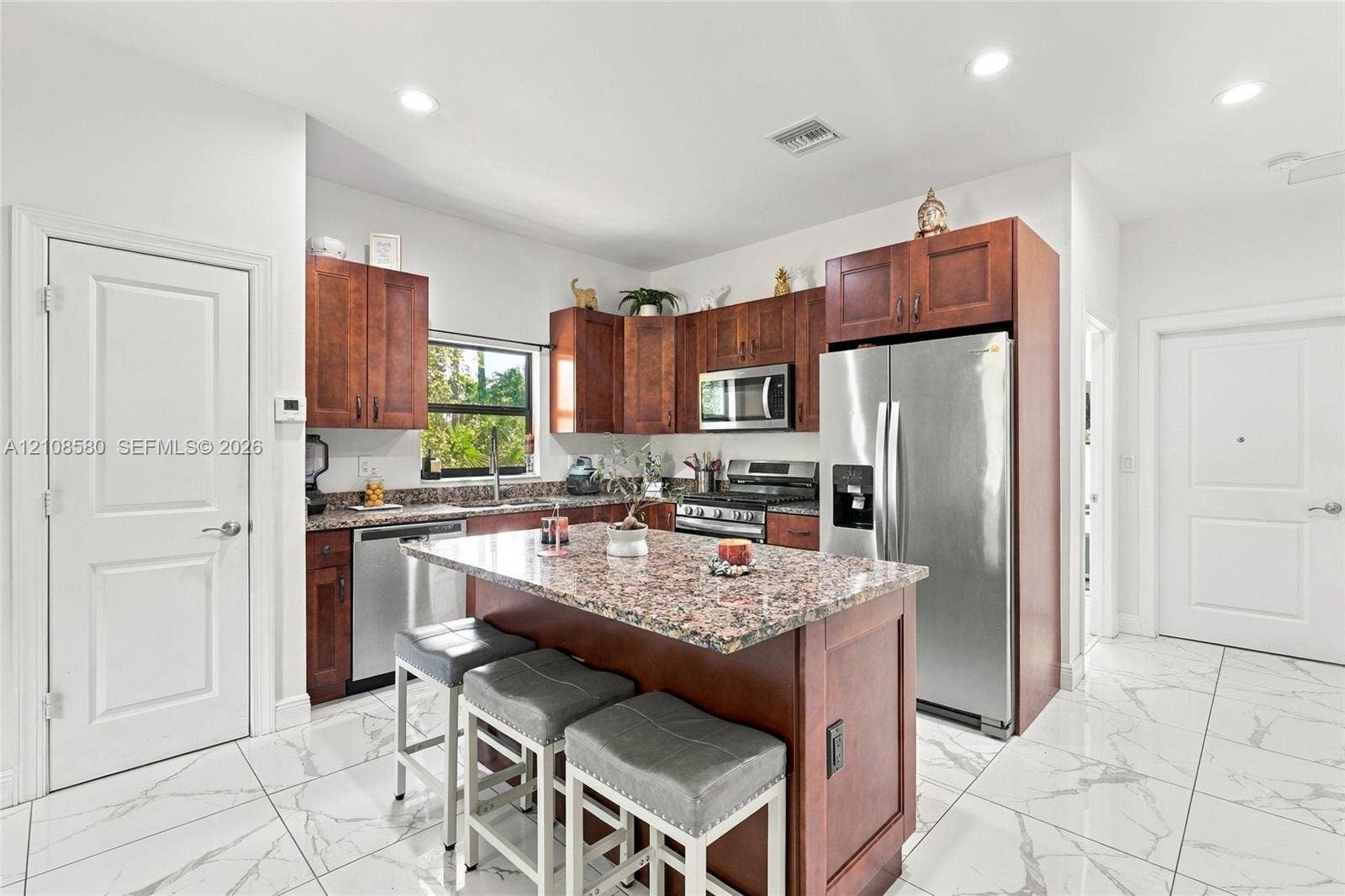 2363 NE 20 Th Avenue, Naples, FL 34120 Kitchen featuring stained wood cabinetry, stone-surface countertops, center island with seating, stainless steel appliances, and large-format tile flooring