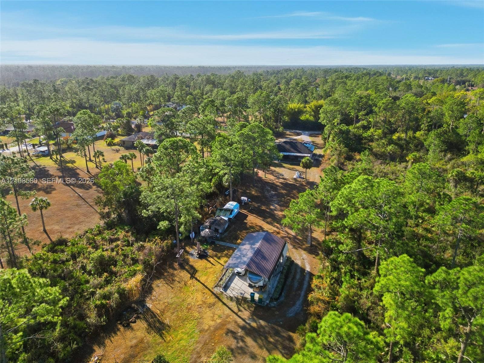 2363 NE 20 Th Avenue, Naples, FL 34120 Aerial perspective featuring a metal-roofed structure with an attached carport, situated on a large, wooded parcel with native vegetation