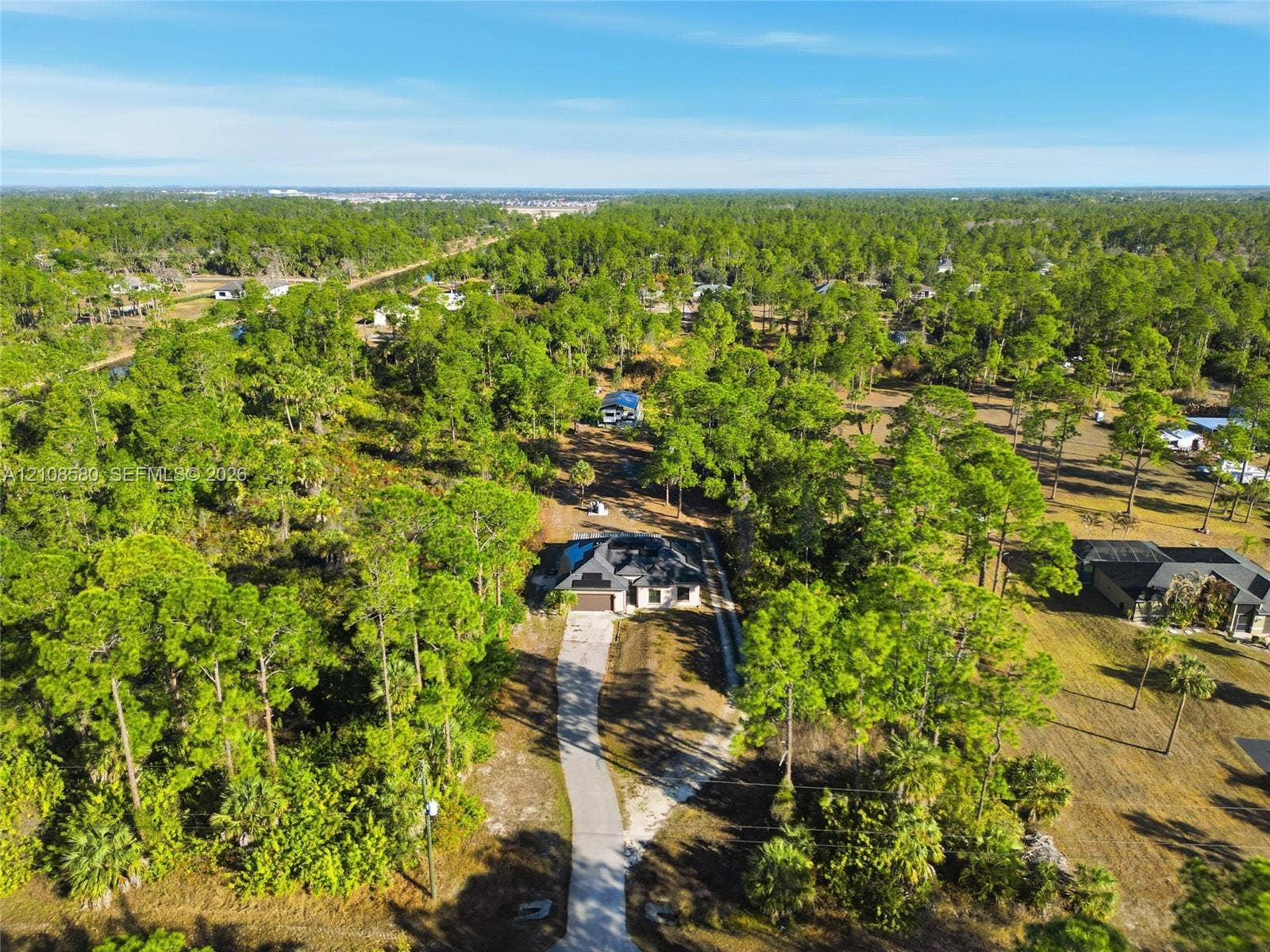2363 NE 20 Th Avenue, Naples, FL 34120 Aerial perspective featuring a single-story residence, a lengthy paved driveway, and extensive surrounding woodland
