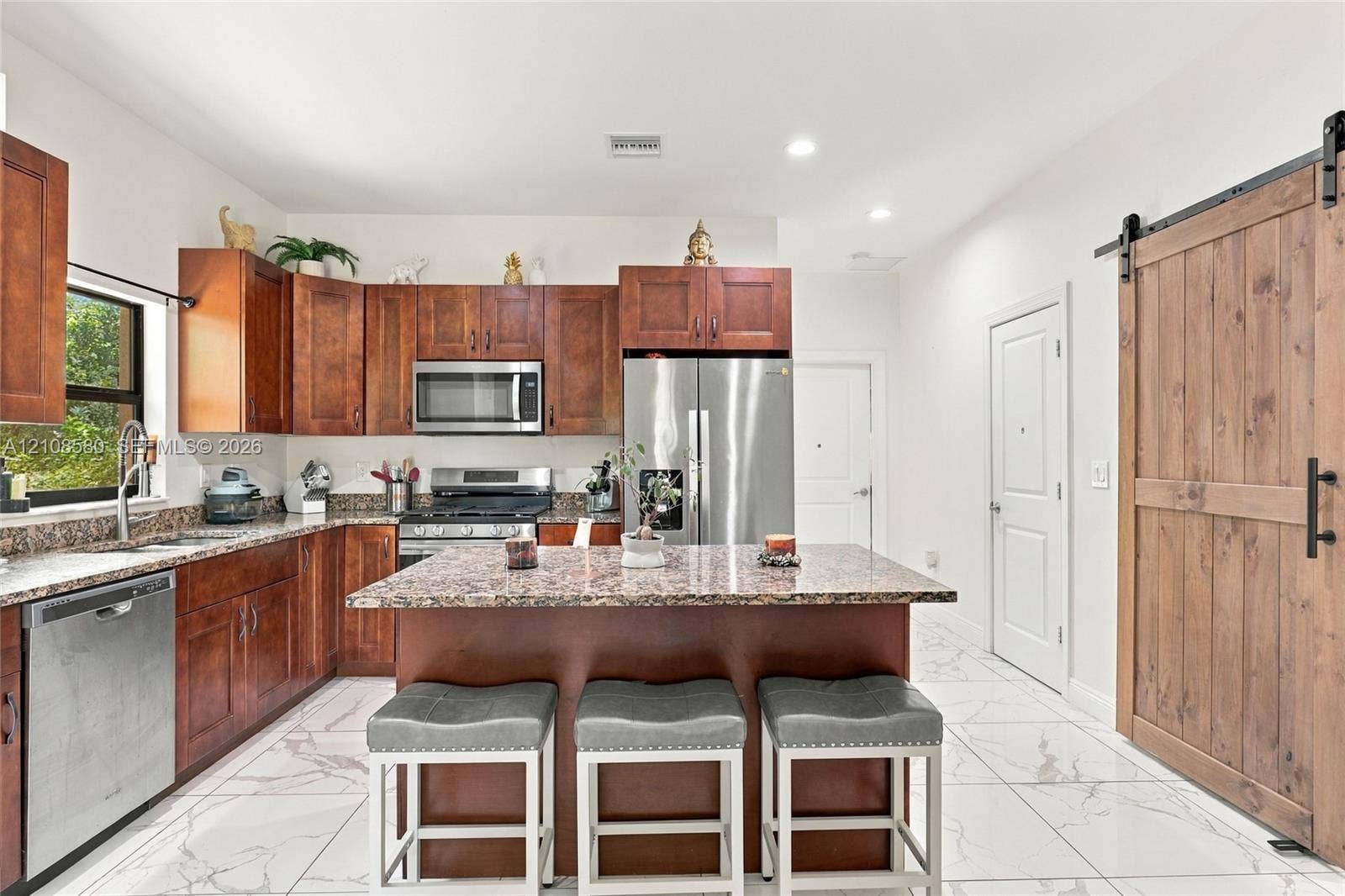 2363 NE 20 Th Avenue, Naples, FL 34120 Kitchen featuring wood cabinetry, stone-surface countertops, stainless steel appliances, a central island, and wood-finish sliding barn door