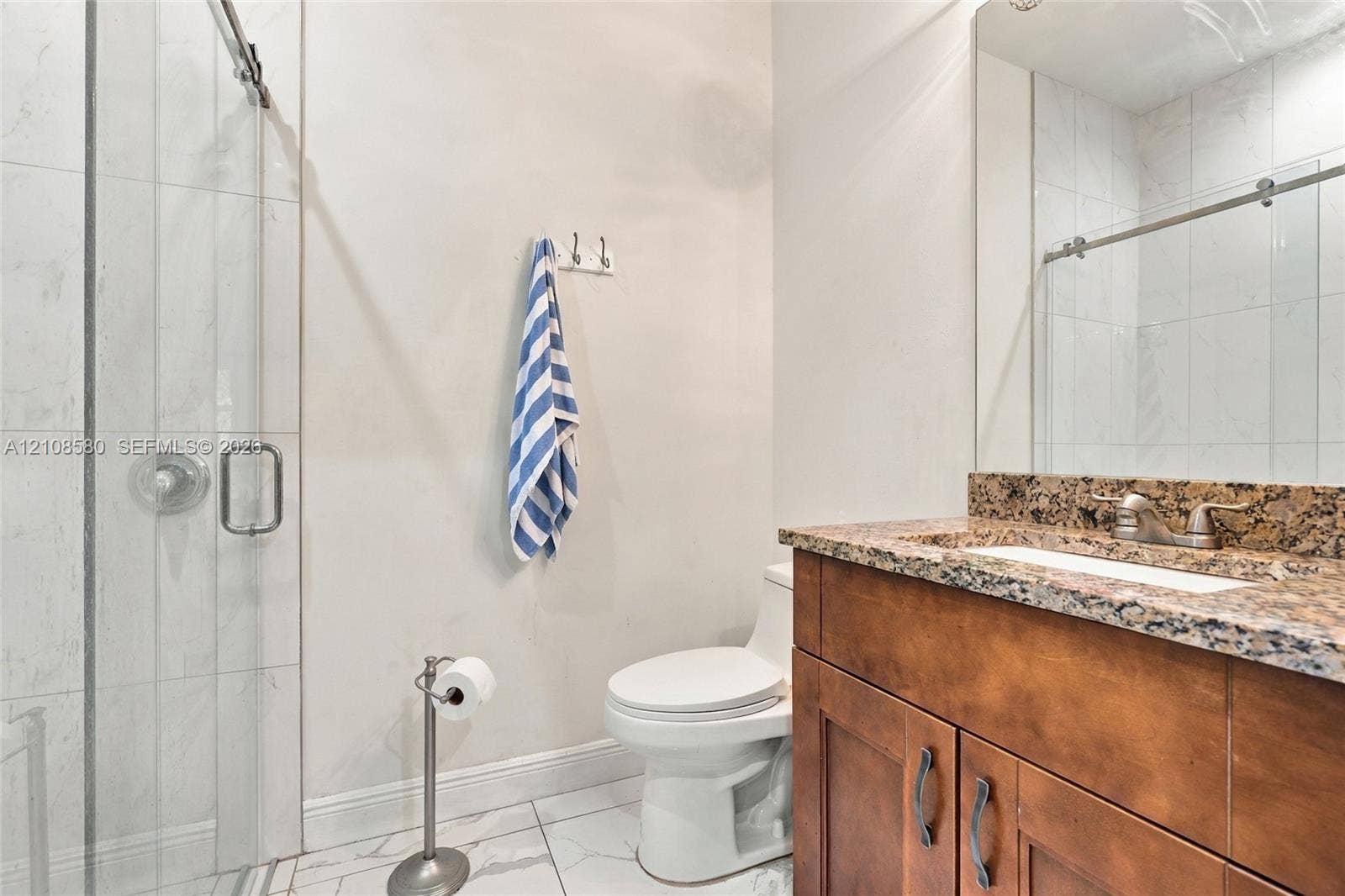 2363 NE 20 Th Avenue, Naples, FL 34120 Bathroom featuring a walk-in shower with glass enclosure, stone-finish countertop, wood-finish vanity cabinetry, and large-format tile flooring