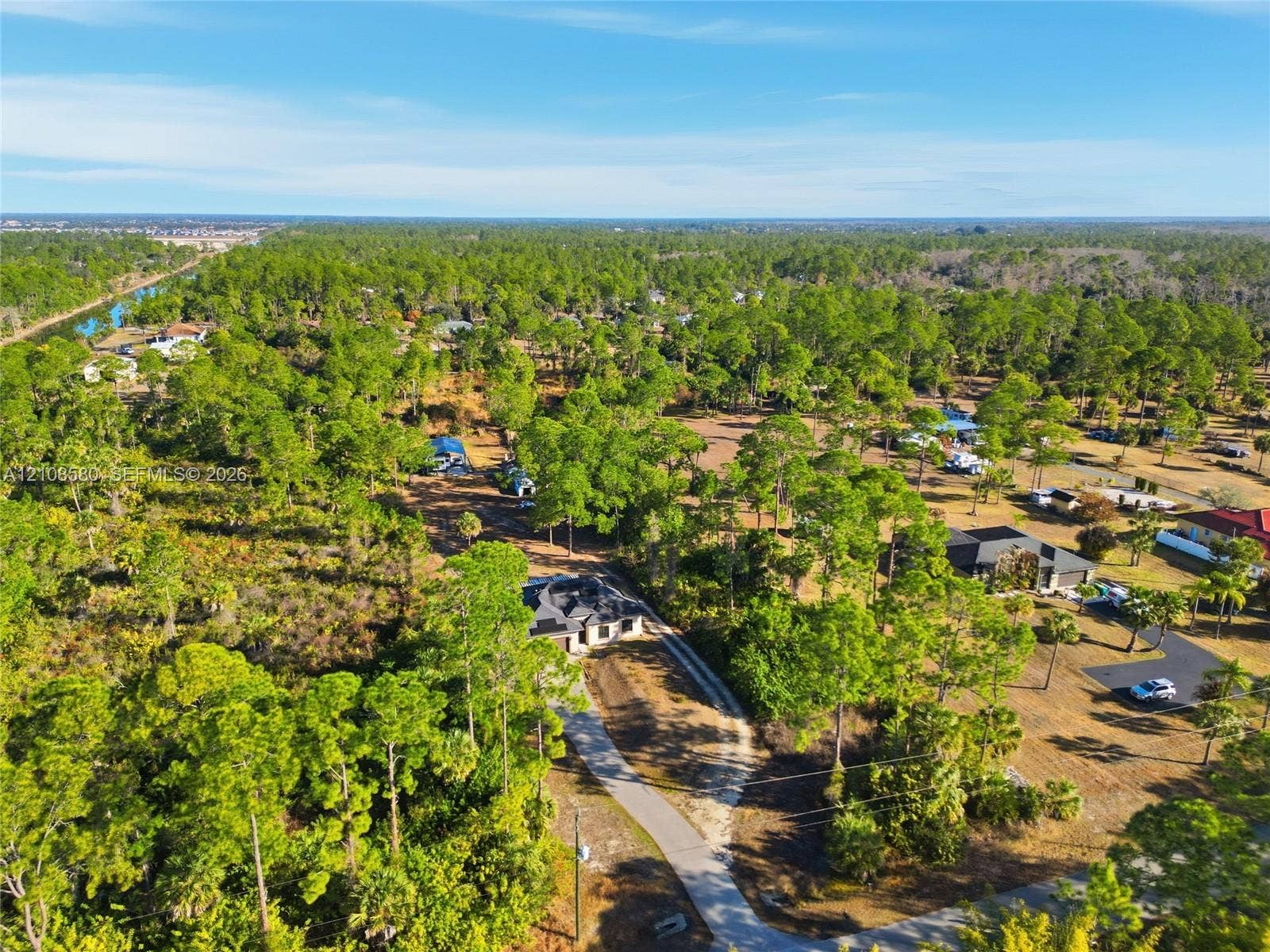 2363 NE 20 Th Avenue, Naples, FL 34120 Aerial perspective of a multi-structure property featuring a pitched-roof dwelling, a paved driveway, and expansive natural acreage with dense mature pine vegetation