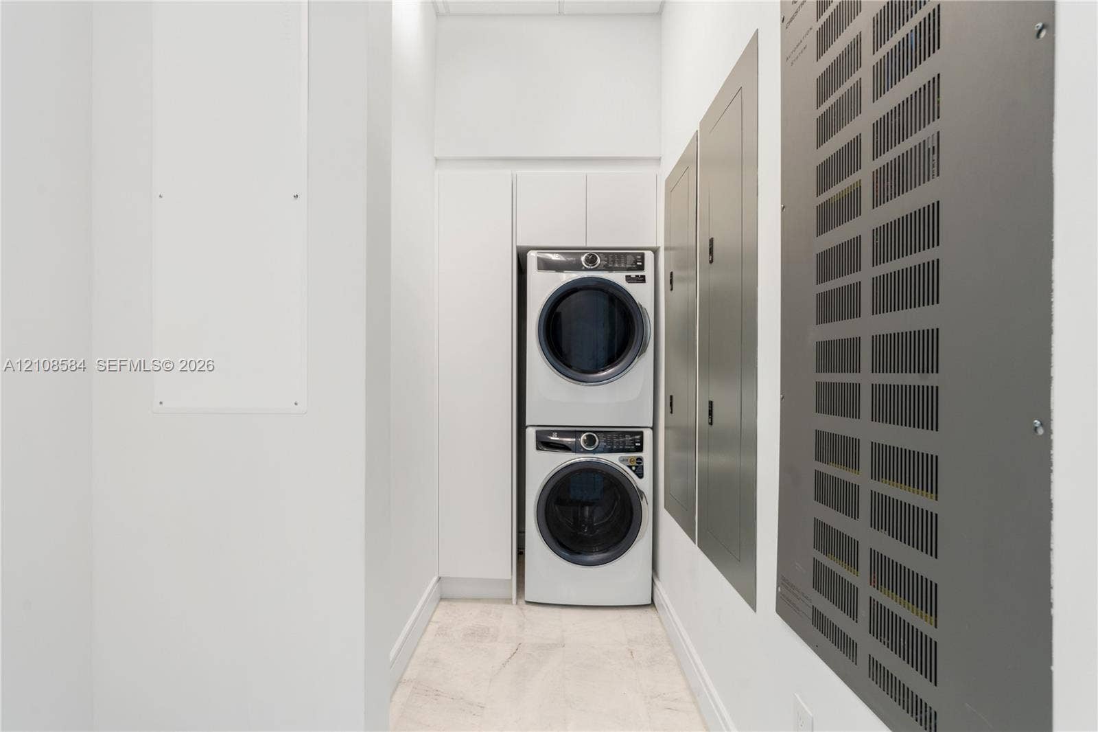 Stacked laundry unit featuring white flat-panel cabinetry and stone-finish flooring