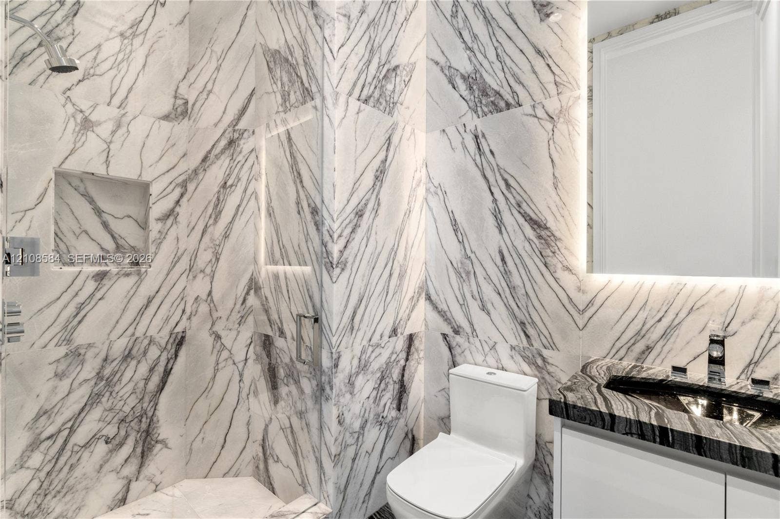 Shower enclosure featuring floor-to-ceiling veined stone tile, a built-in recessed niche, and a glass partition
