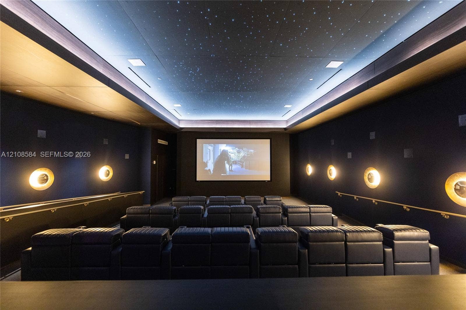 Media room featuring a starlit tray ceiling, tiered seating platforms, circular wall sconces, and metal handrails