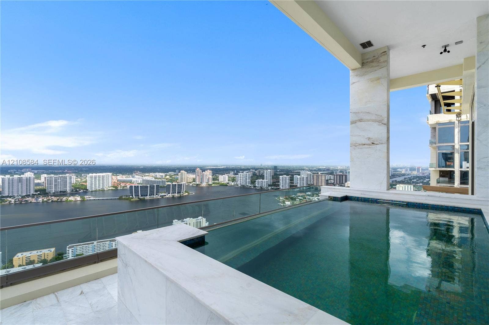 Covered terrace featuring a private infinity-edge plunge pool, stone flooring, and expansive glass railings