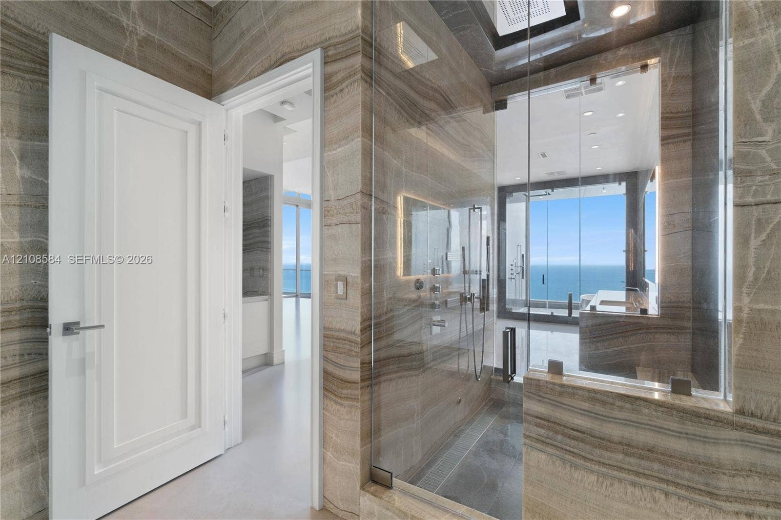 Floor-to-ceiling stone wall cladding, walk-in glass-enclosed shower with wall-mounted fixtures, and recessed ceiling lighting