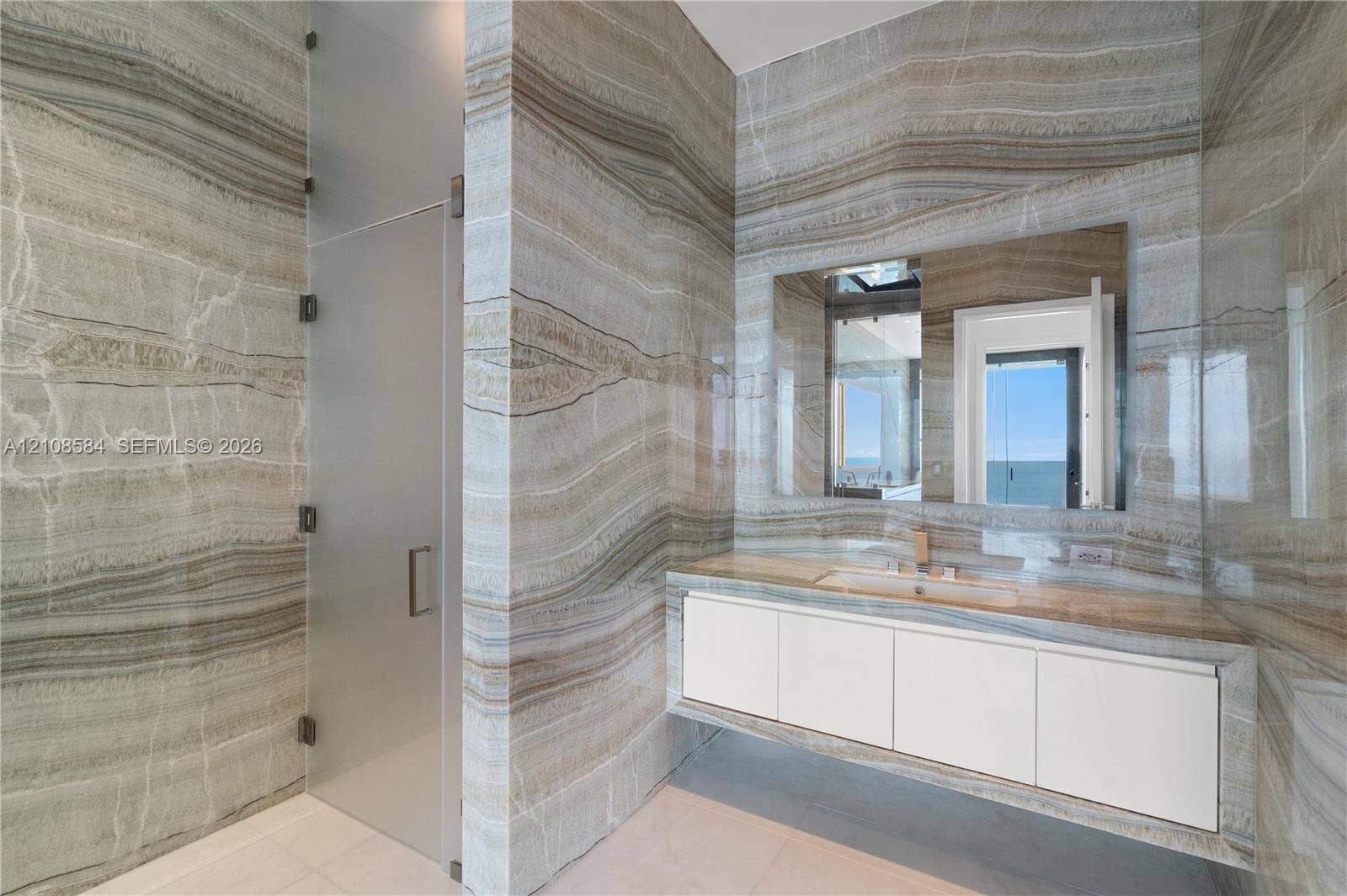 Floor-to-ceiling natural stone wall cladding, floating vanity with integrated stone sink, polished metal faucet, and frameless glass shower enclosure