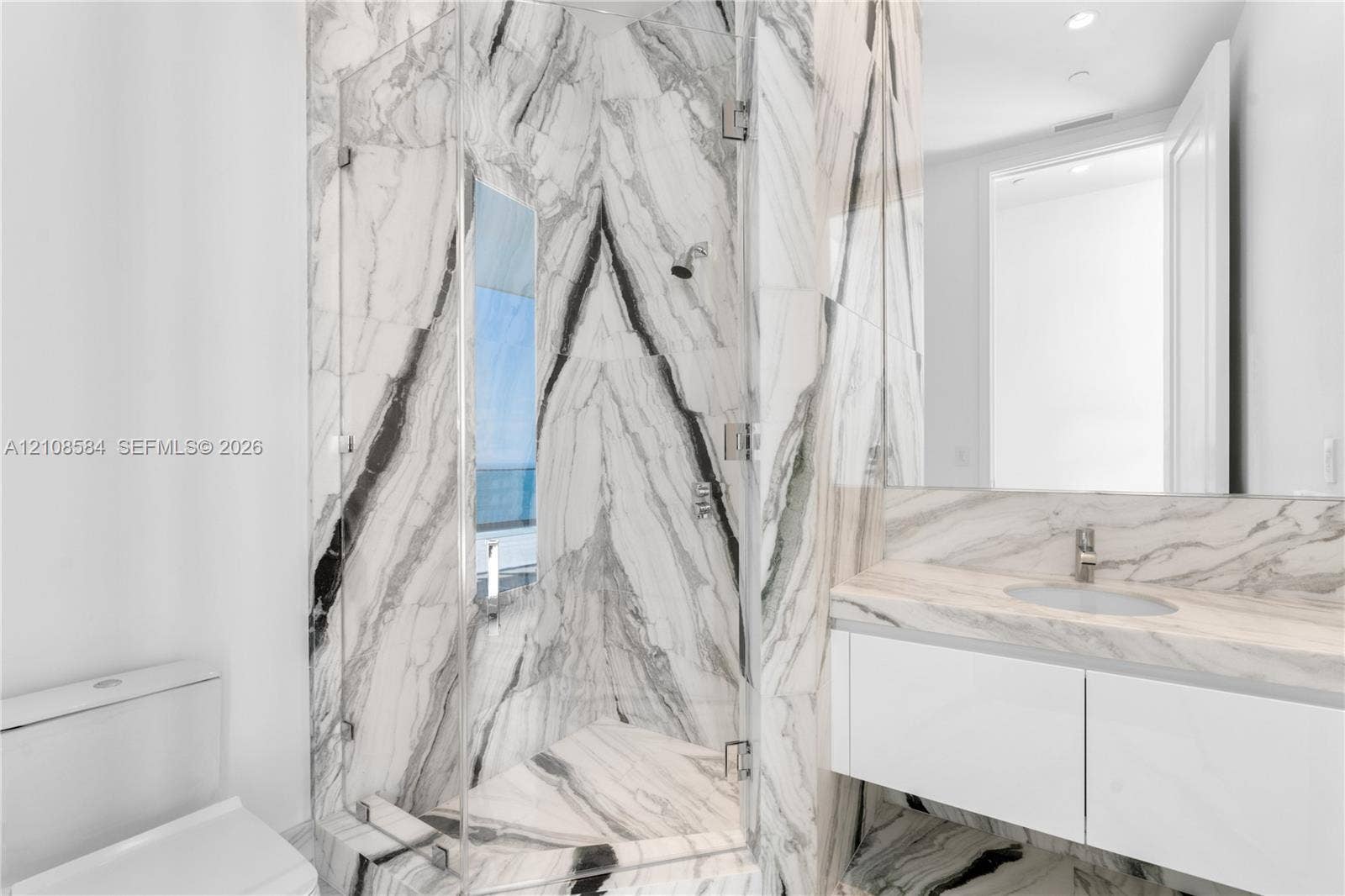 Full-height stone wall tiling, glass-enclosed shower, wall-mounted floating vanity, integrated countertop with oval basin, and expansive wall-mounted mirror