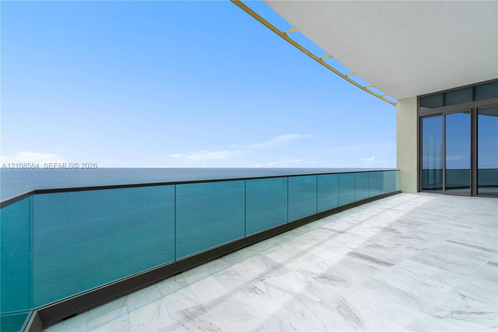 Covered balcony featuring stone flooring, a structural glass railing, and dark-frame sliding glass doors