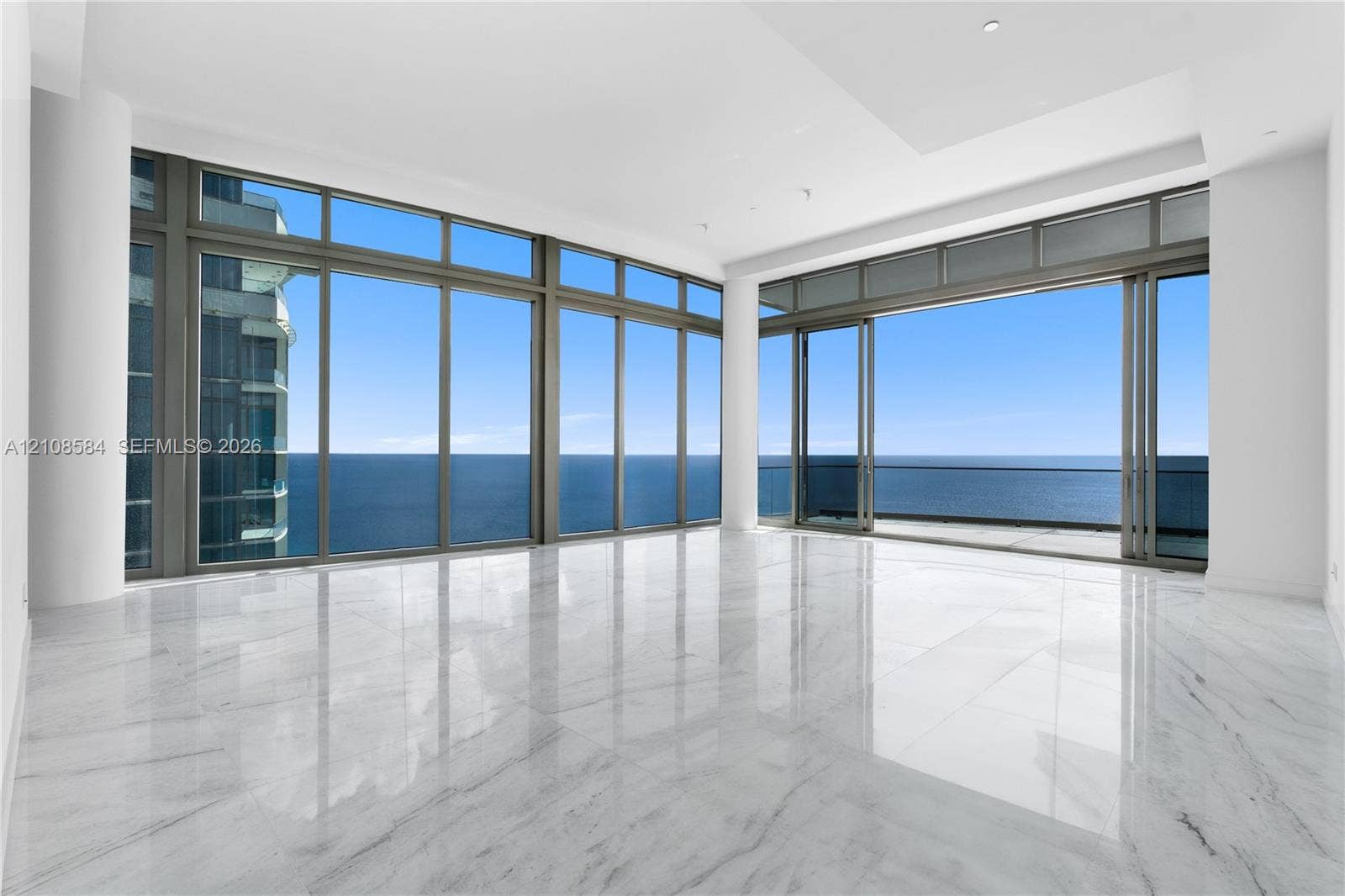 Floor-to-ceiling glass walls, polished stone flooring, recessed lighting, and a private balcony featuring an ocean backdrop