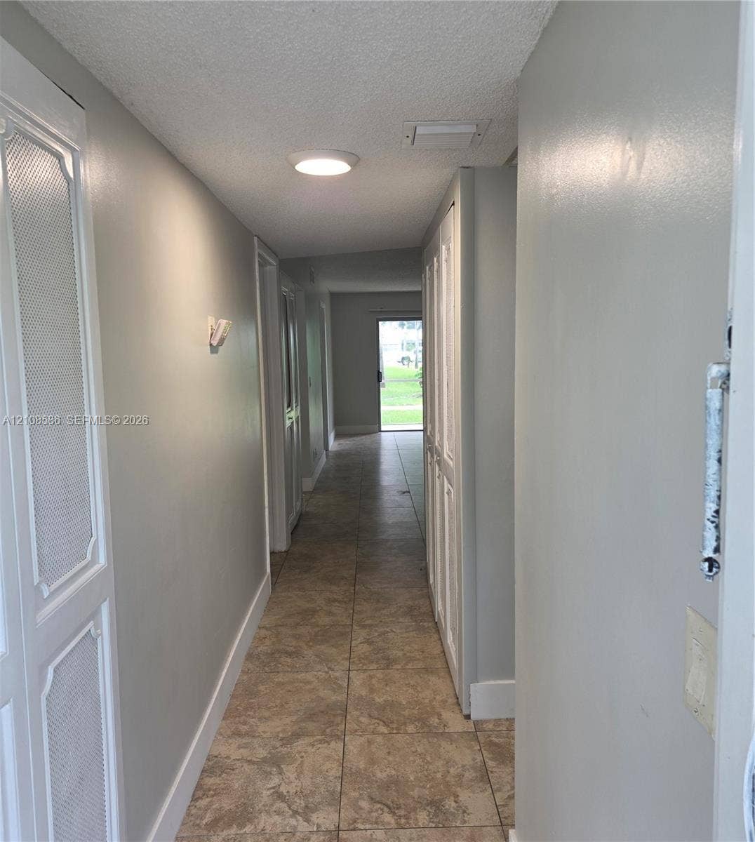 6075 N Sabal Palm Boulevard, #110, Tamarac, FL 33319 Hallway featuring large-format ceramic tile flooring, built-in floor-to-ceiling storage cabinetry with louvered doors, and flush-mount ceiling lighting