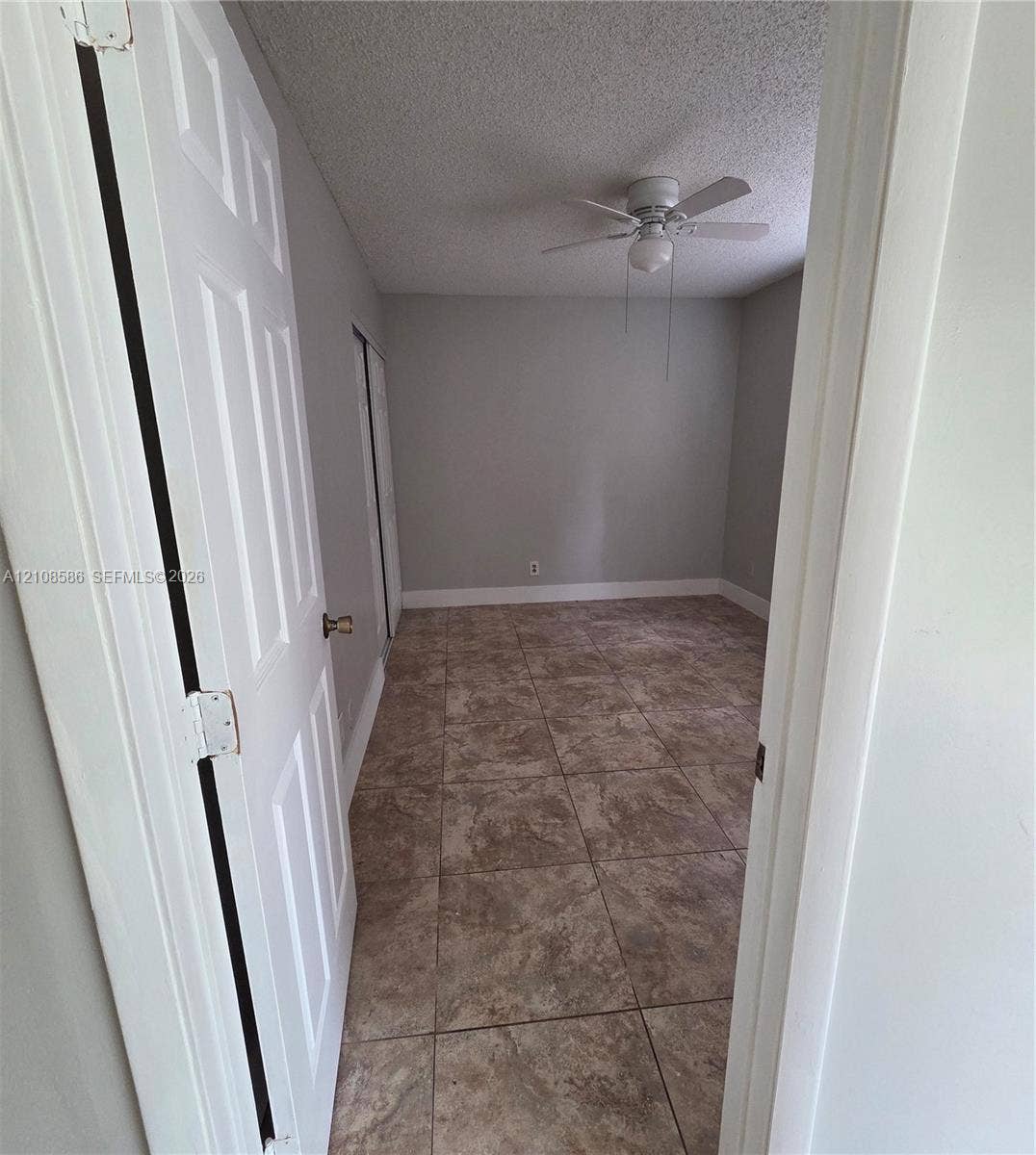 6075 N Sabal Palm Boulevard, #110, Tamarac, FL 33319 Neutral-toned interior space featuring stone-style tile flooring, white six-panel doors, and a ceiling-mounted light fixture with integrated fan