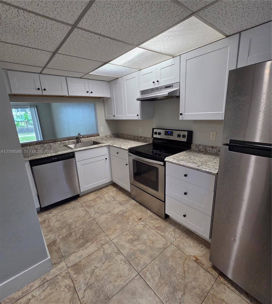 6075 N Sabal Palm Boulevard, #110, Tamarac, FL 33319 Kitchen featuring white shaker-style cabinetry, stone-patterned countertops, stainless steel appliances, and tile flooring