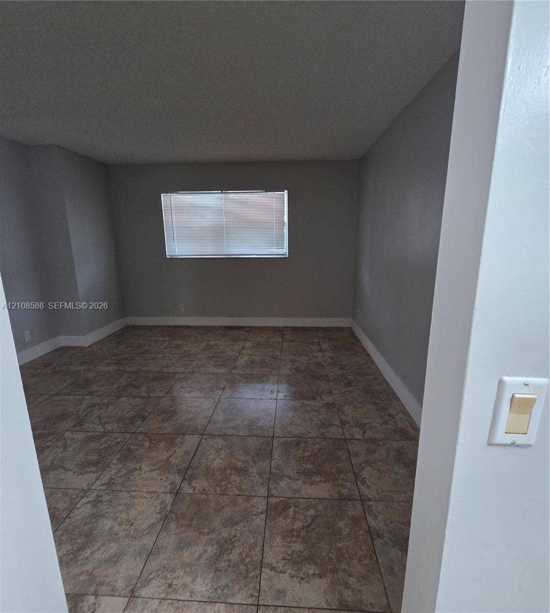 6075 N Sabal Palm Boulevard, #110, Tamarac, FL 33319 Interior space featuring neutral wall paint, large-format tile flooring, and a window with integrated blinds