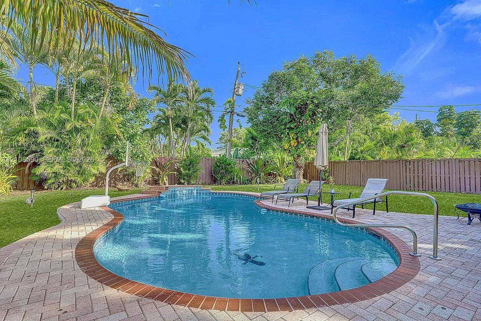 In-ground swimming pool featuring a brick paver surround, integrated entry steps, and metal handrails, complemented by a grass lawn and privacy fencing