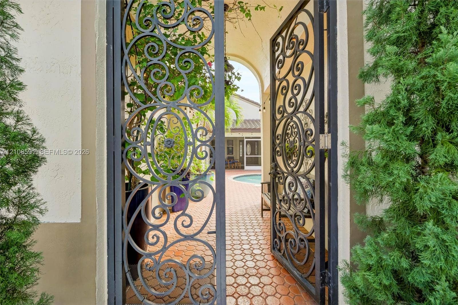 415 SW 200th Terrace, Pembroke Pines, FL 33029 Decorative wrought-iron entry gate featuring intricate scrollwork, opening to a paved courtyard with a pool area