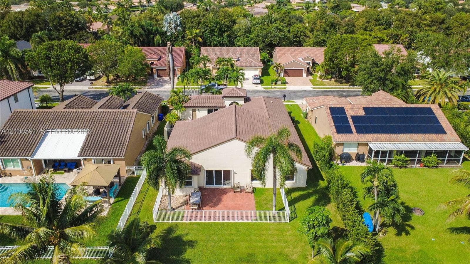 415 SW 200th Terrace, Pembroke Pines, FL 33029 Aerial perspective featuring a neutral-toned stucco exterior, a multi-pitched roof, a paved patio, and a fenced yard with mature landscaping