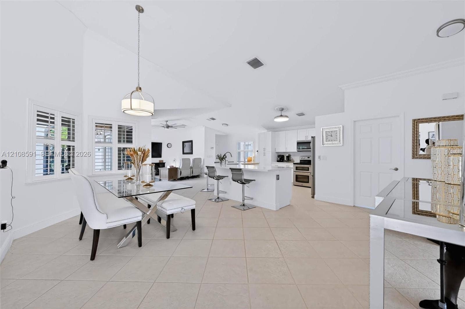 415 SW 200th Terrace, Pembroke Pines, FL 33029 Open-concept interior featuring vaulted ceilings, tile flooring, a kitchen island with stone-finish countertops, crisp white cabinetry, and plantation shutters
