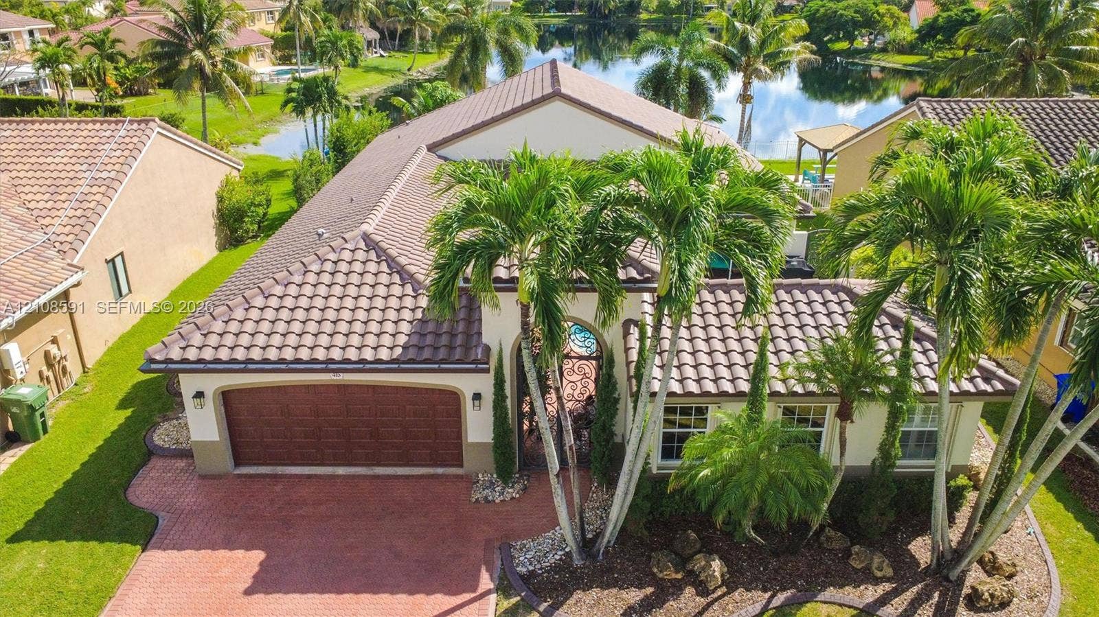 415 SW 200th Terrace, Pembroke Pines, FL 33029 Single-story residence featuring a tile roof, brick-paver driveway, arched entryway, and waterfront location with established palm landscaping