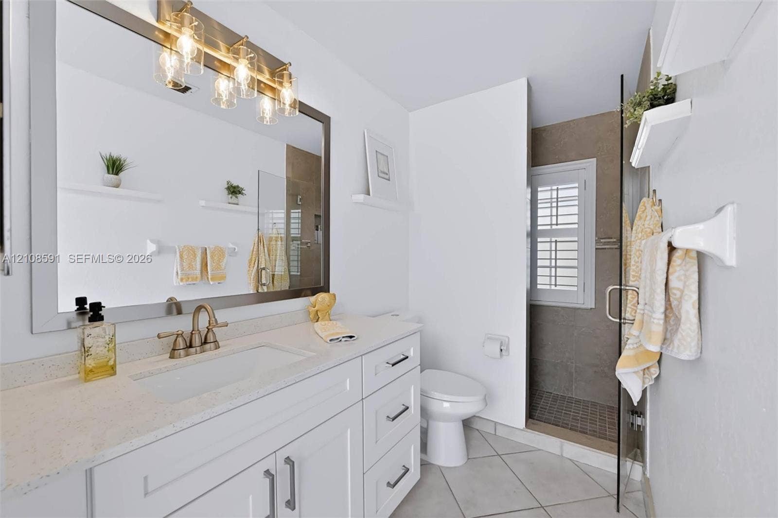 415 SW 200th Terrace, Pembroke Pines, FL 33029 Bathroom vanity featuring white shaker-style cabinetry, a light-toned solid surface countertop, an integrated rectangular sink, a multi-light fixture, and a walk-in shower with a glass door and neutral wall tile