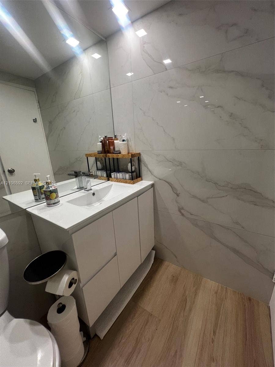 10185 Collins Avenue, #515, Bal Harbour, Bal Harbour, FL 33154 White vanity with integrated rectangular sink and polished chrome faucet, large-format veined wall tile, wood-finish flooring, and wall-to-wall mirror