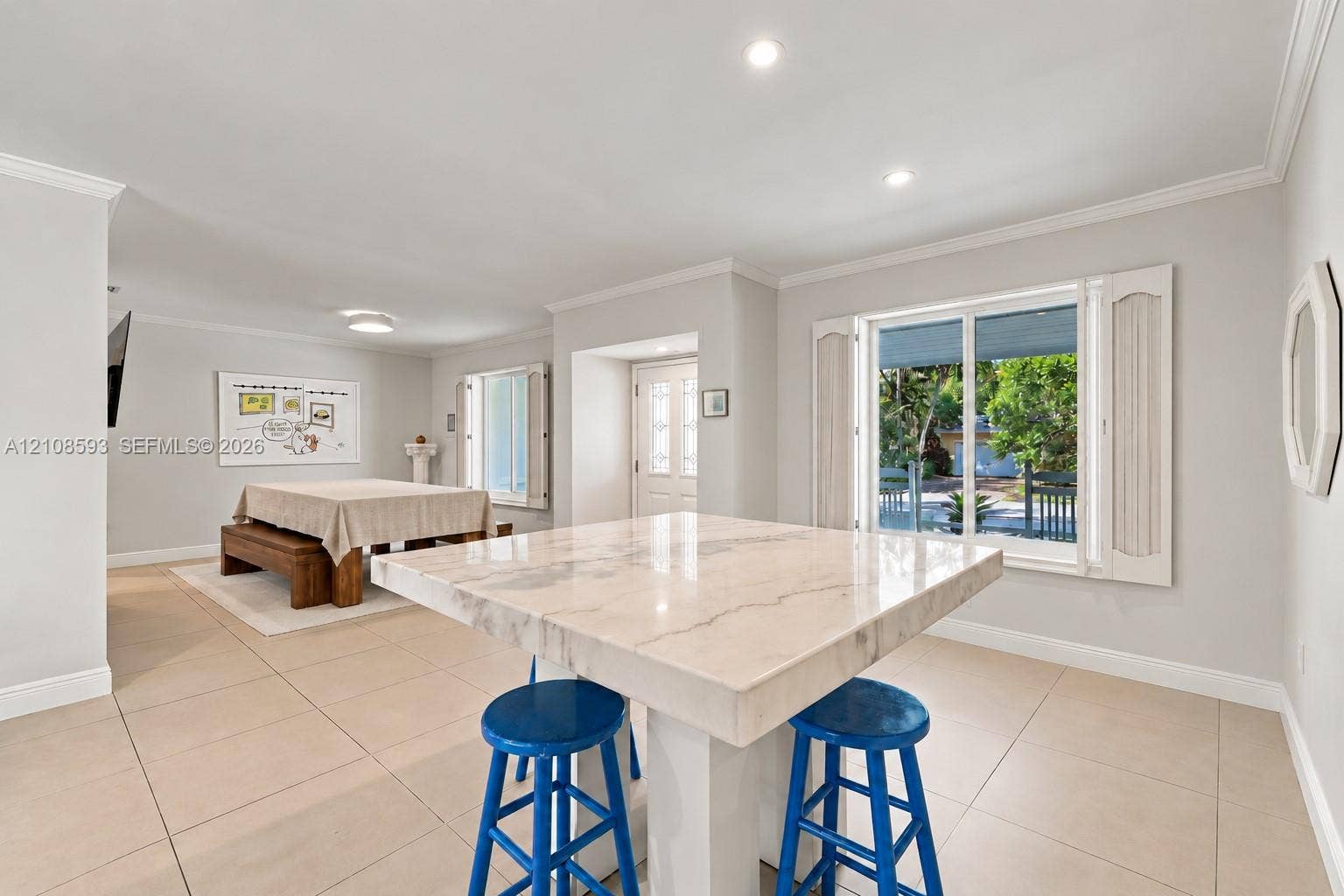 8230 SW 151st Street, Palmetto Bay, FL 33158 Open-concept interior featuring large-format tile flooring, recessed ceiling lighting, a central stone-top island, and dual windows equipped with plantation shutters