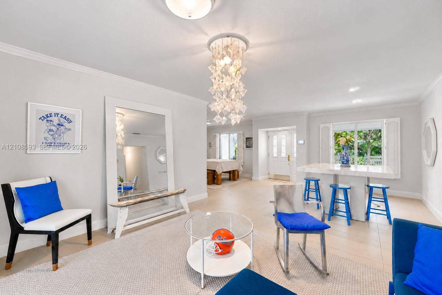8230 SW 151st Street, Palmetto Bay, FL 33158 Open-concept interior featuring large-format tile flooring, a multi-tiered crystal-style chandelier, decorative crown molding, and a built-in stone-top island