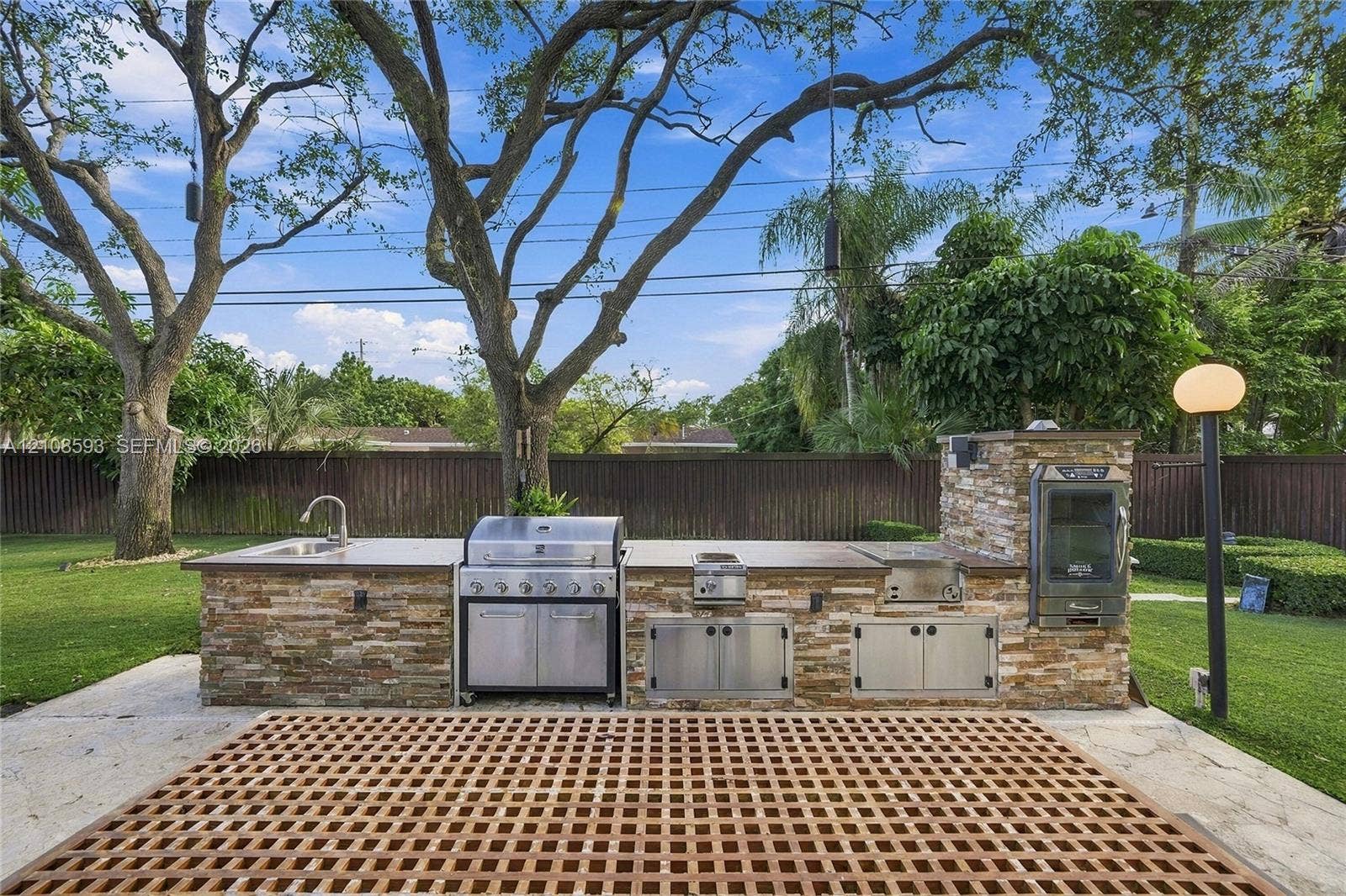 8230 SW 151st Street, Palmetto Bay, FL 33158 Outdoor kitchen featuring stacked stone cladding, stainless steel grill and storage cabinetry, built-in smoker, and integrated sink