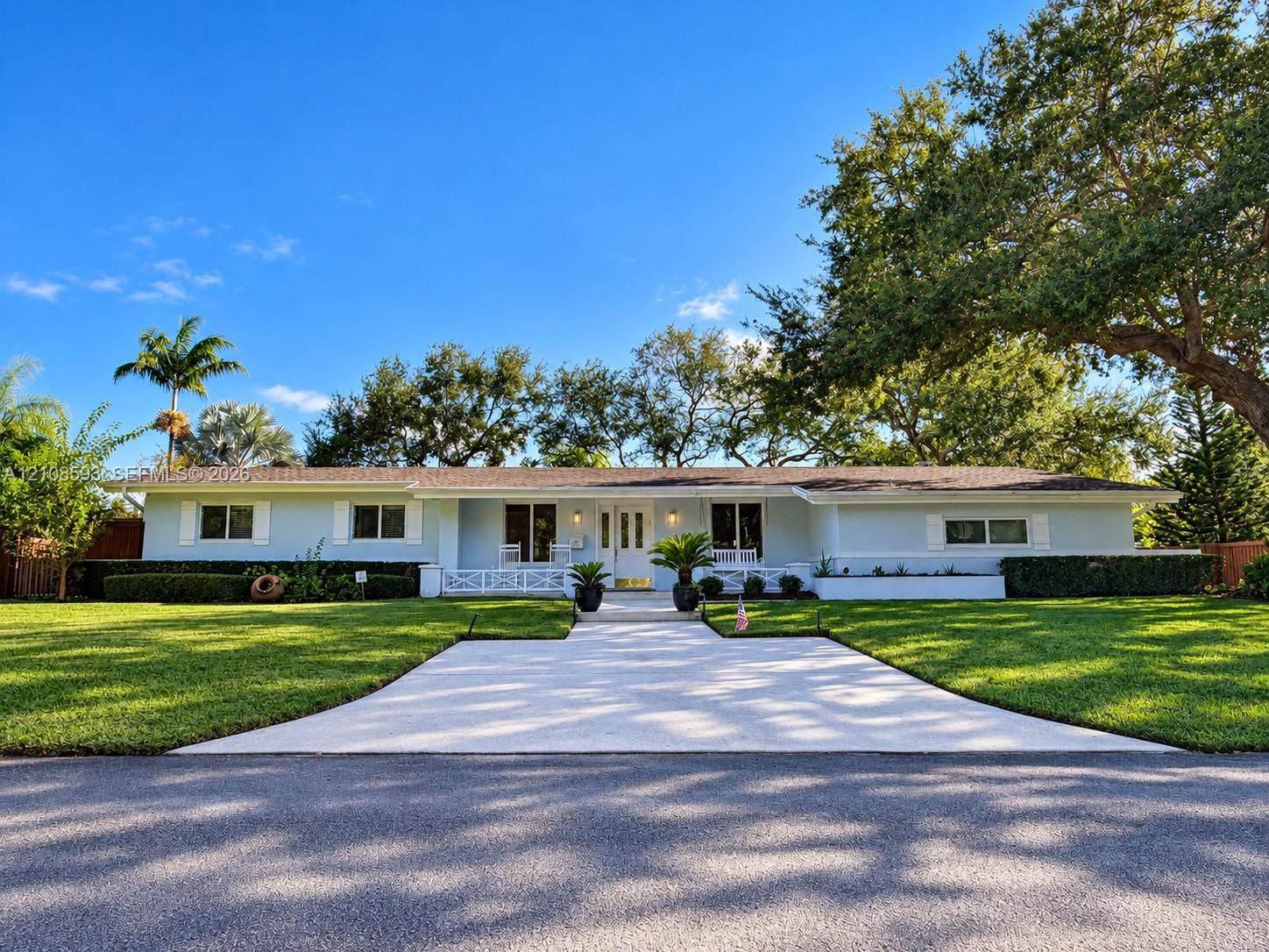 8230 SW 151st Street, Palmetto Bay, FL 33158 Single-story residence featuring light-toned exterior cladding, a paved walkway, covered front porch with decorative railing, and manicured landscaping