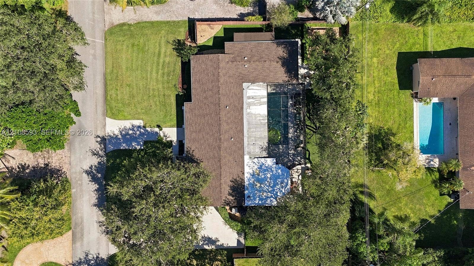 8230 SW 151st Street, Palmetto Bay, FL 33158 Aerial perspective featuring a multi-pitched shingle roof, paved driveway, expansive lawn, and mature trees