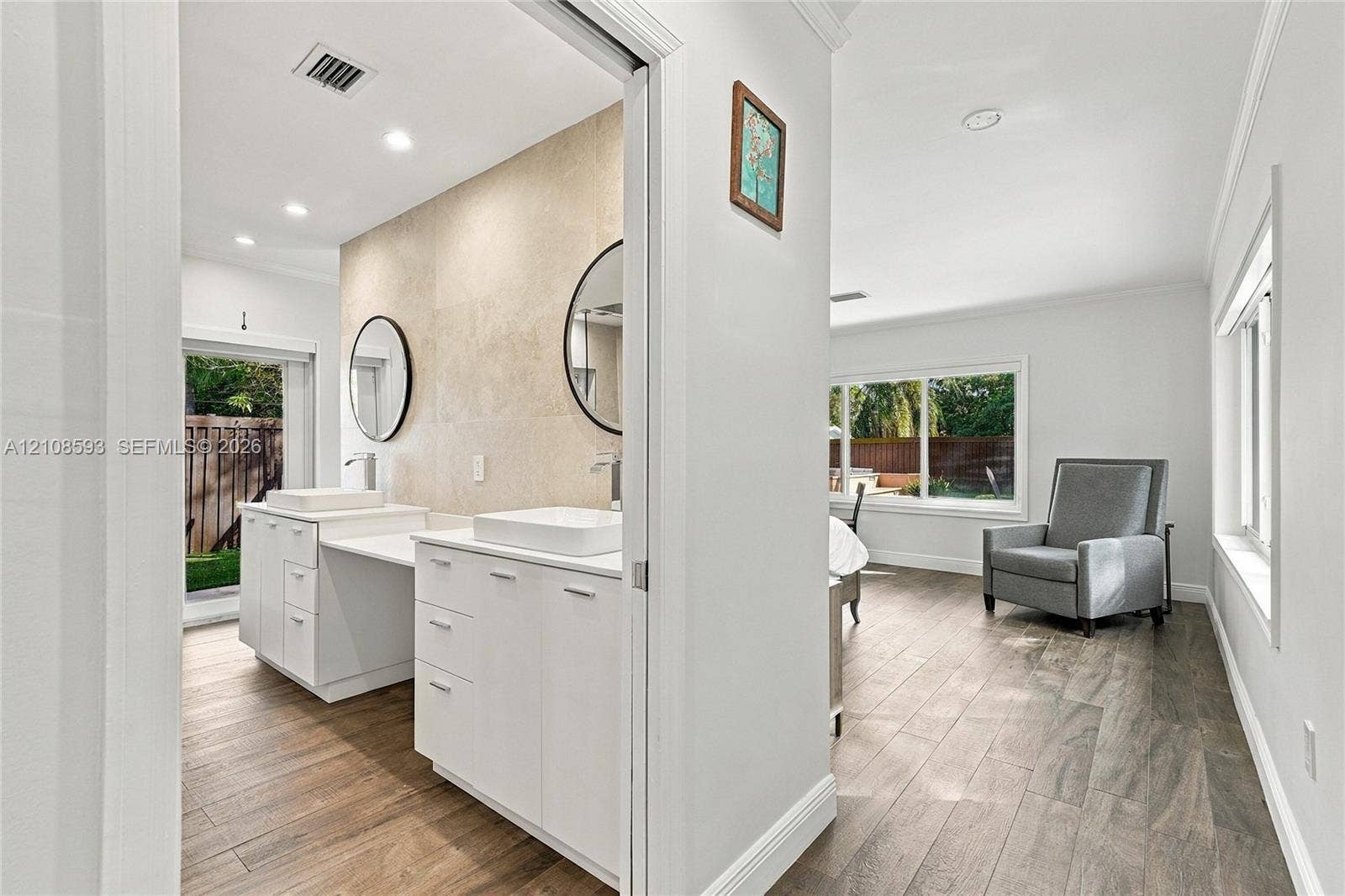 8230 SW 151st Street, Palmetto Bay, FL 33158 Double vanity featuring white cabinetry, square vessel sinks, and stone-tiled backsplash with circular wall-mounted mirrors and wood-finish flooring