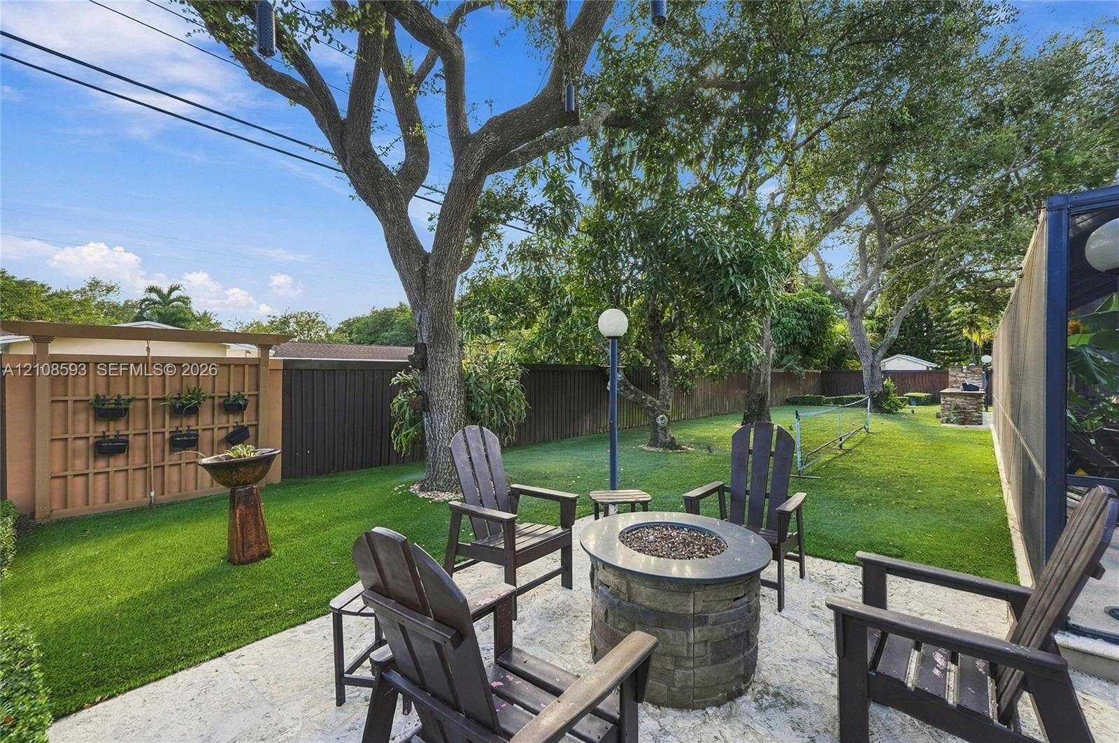 8230 SW 151st Street, Palmetto Bay, FL 33158 Backyard featuring a stone-paver patio, built-in circular stone fire pit, wood-lattice privacy screen, and mature trees