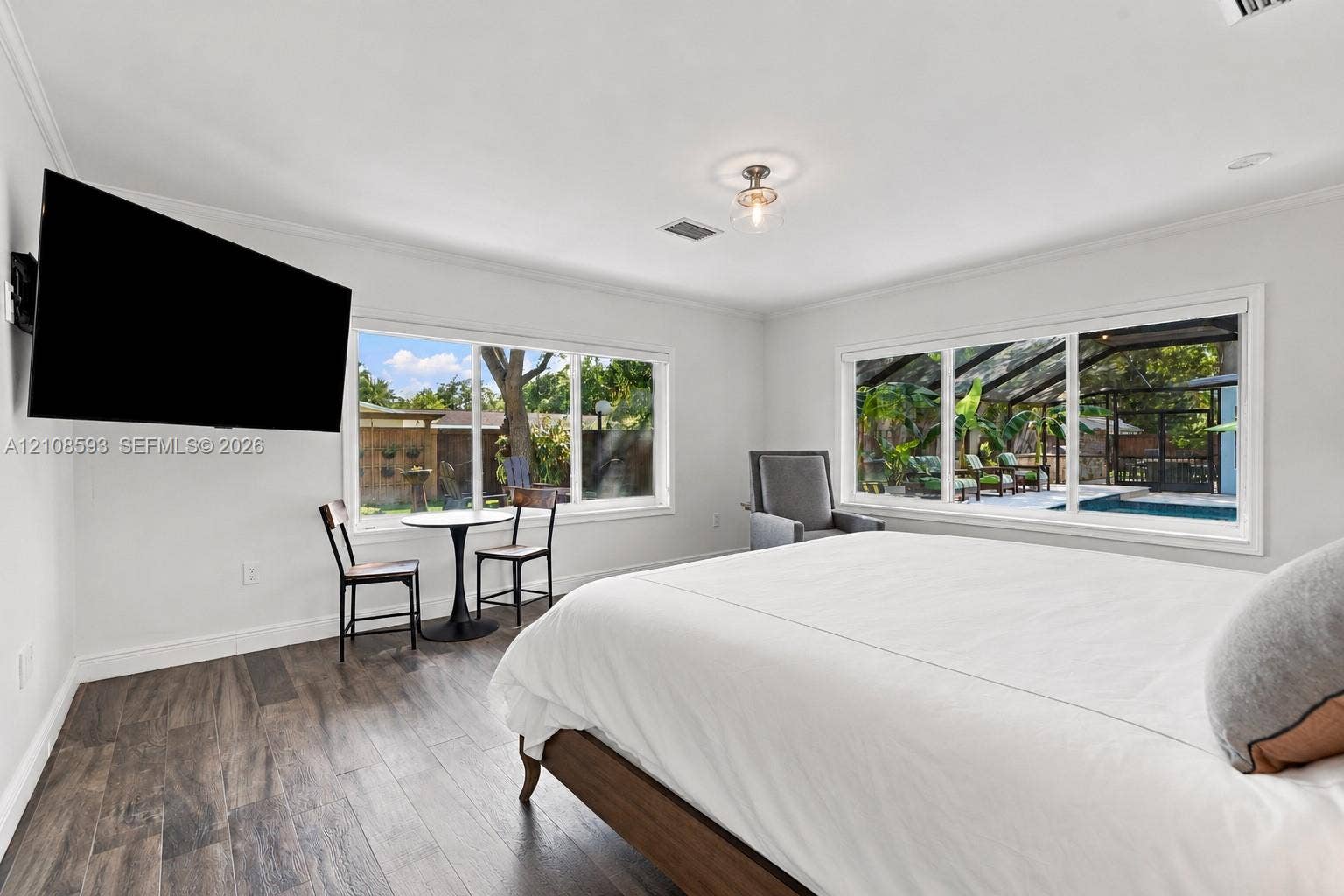 8230 SW 151st Street, Palmetto Bay, FL 33158 Neutral-toned interior featuring wood-finish flooring, dual large-scale windows with natural light, a semi-flush mount ceiling fixture, and crown molding