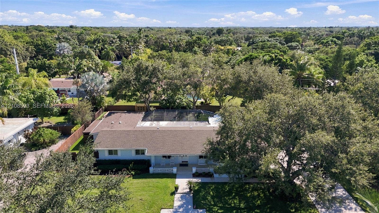 8230 SW 151st Street, Palmetto Bay, FL 33158 Aerial perspective featuring a single-story residence with a multi-hipped roof, a screened-in rear enclosure, a paved driveway, and mature landscaping on an expansive lot