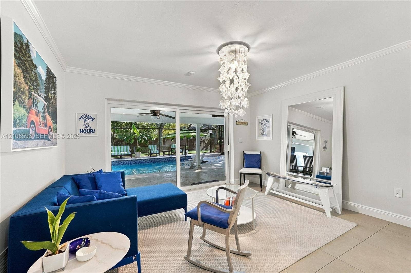 8230 SW 151st Street, Palmetto Bay, FL 33158 Interior space featuring crown molding, large-format tile flooring, a tiered crystal chandelier, and sliding glass doors revealing a screened-in pool