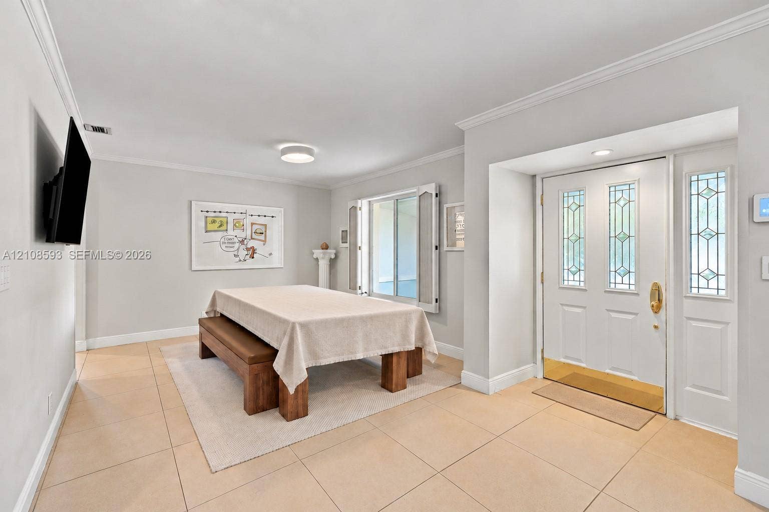 8230 SW 151st Street, Palmetto Bay, FL 33158 Entryway featuring neutral-tone tile flooring, crown molding, and a white front door with decorative glass inserts, brass hardware, and a matching sidelight