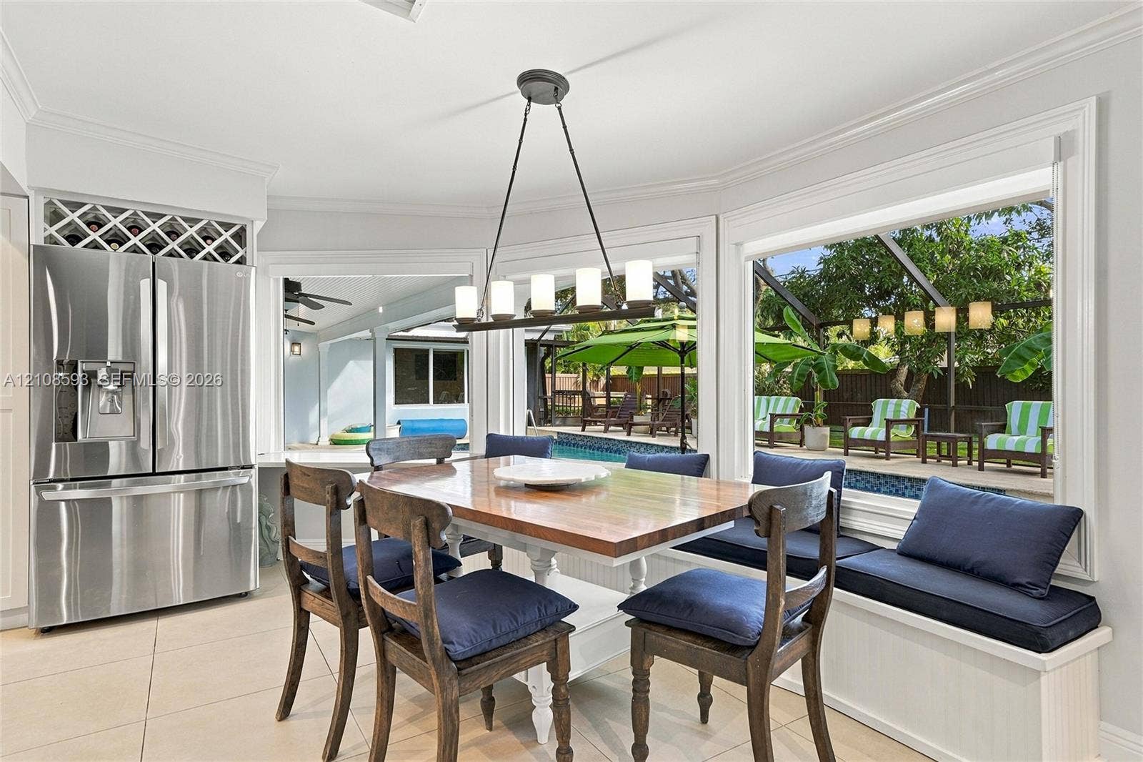 8230 SW 151st Street, Palmetto Bay, FL 33158 Dining area featuring large-format tile flooring, built-in window seating with integrated storage, stainless steel refrigerator with overhead wine rack, and a linear pendant light fixture