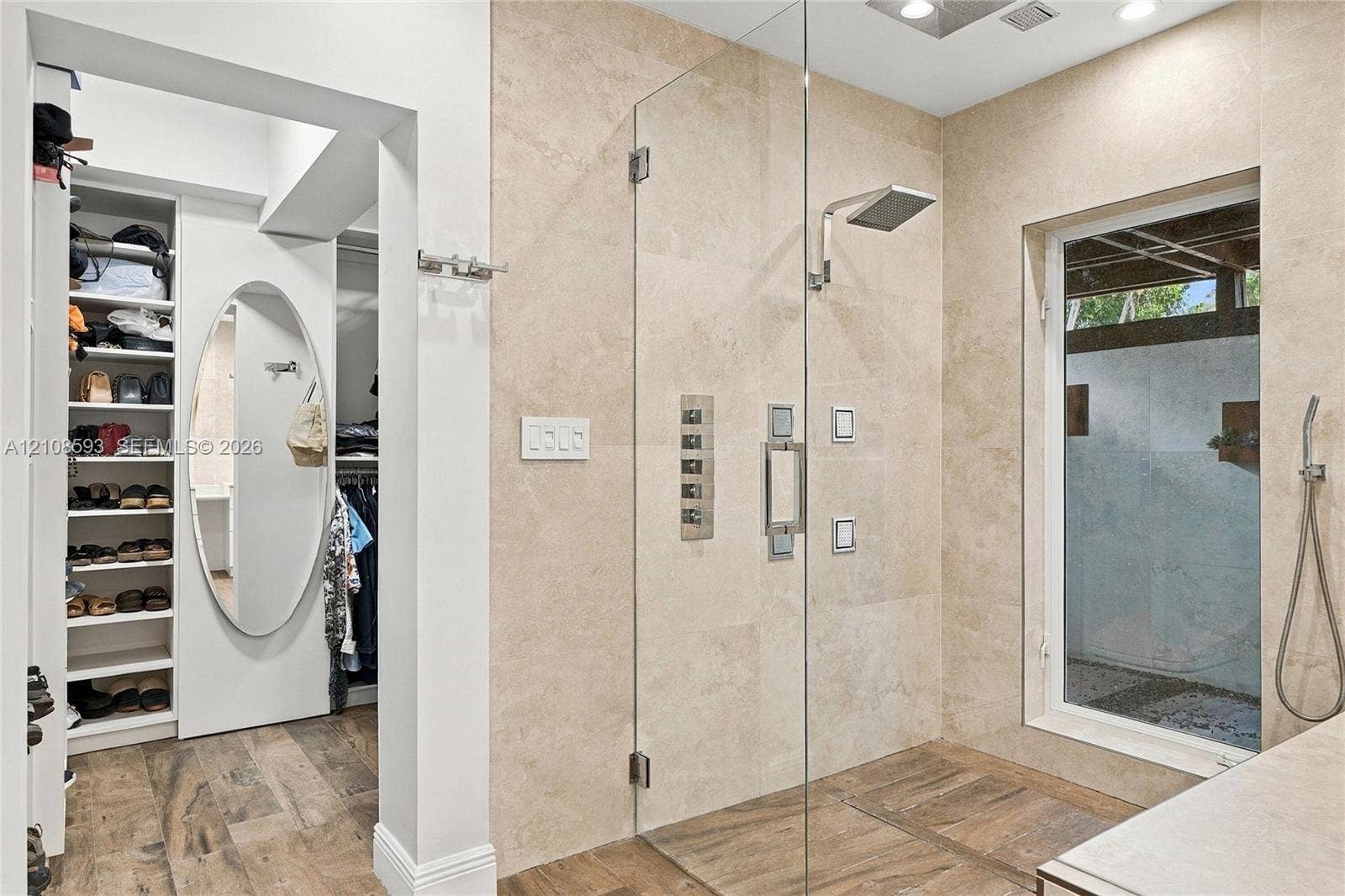 8230 SW 151st Street, Palmetto Bay, FL 33158 Walk-in shower featuring floor-to-ceiling stone tile, a glass enclosure, a rainfall showerhead, and a wall-mounted hand shower, paired with a built-in closet system