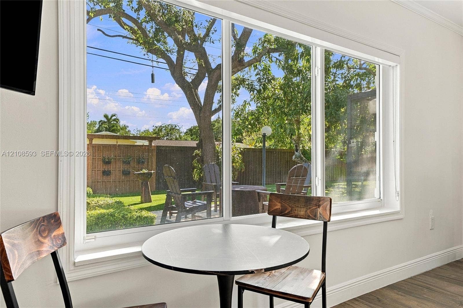 8230 SW 151st Street, Palmetto Bay, FL 33158 Large-scale picture window with white trim, wood-finish flooring, and backyard access featuring a wood privacy fence and mature landscaping