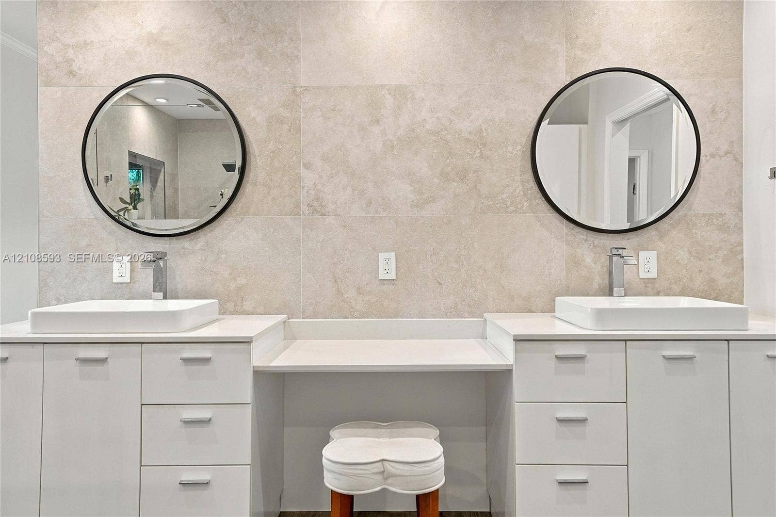 8230 SW 151st Street, Palmetto Bay, FL 33158 Dual white cabinetry with white stone countertops, integrated center vanity station, dual vessel sinks, wall-mounted round mirrors with matte black frames, and neutral tile wall surround