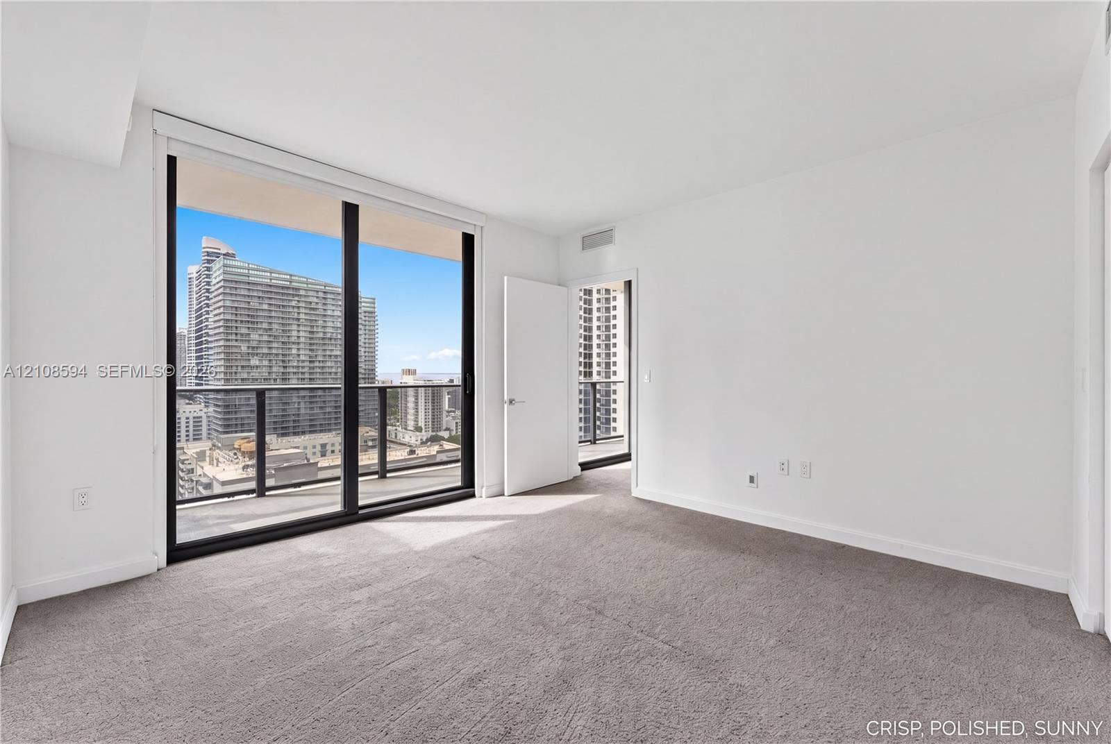 45 SW 9th Street, #2206, Miami, FL 33130 Floor-to-ceiling glass sliding doors, private balcony with metal railing, carpeted flooring, and urban cityscape scenery
