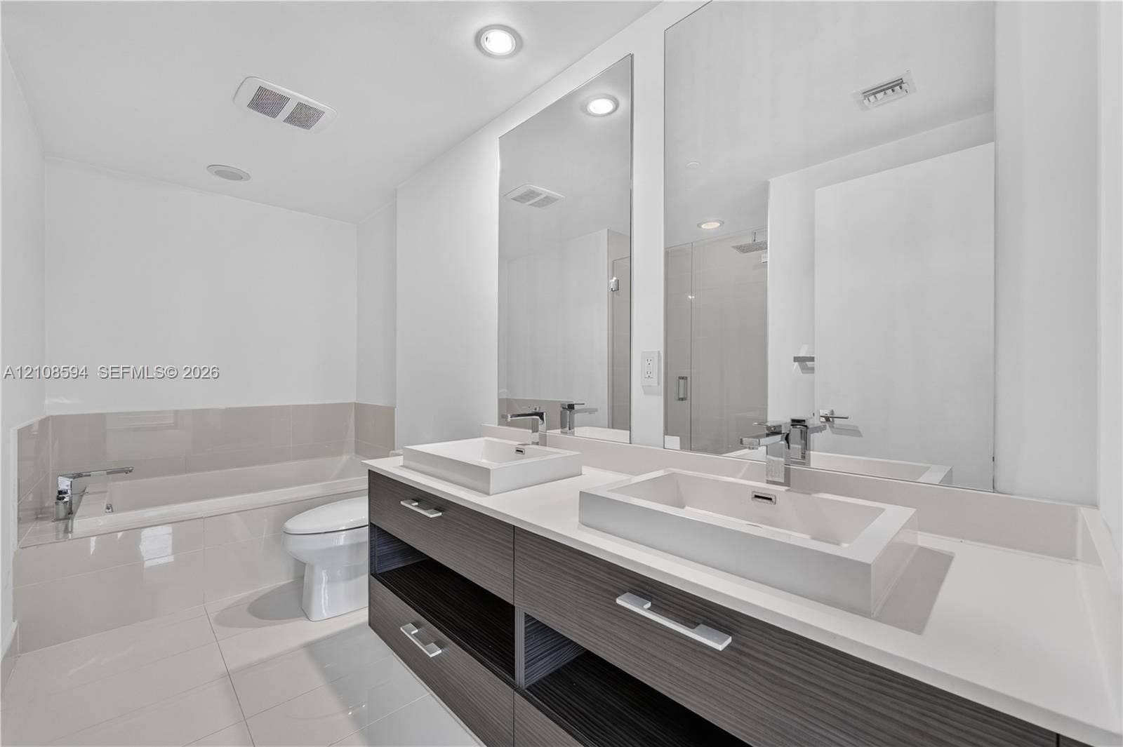 45 SW 9th Street, #2206, Miami, FL 33130 Modern floating vanity featuring dual rectangular vessel sinks, a solid surface countertop, wood-finish cabinetry, and polished chrome fixtures, complemented by floor-to-ceiling mirrors and a deep soaking tub